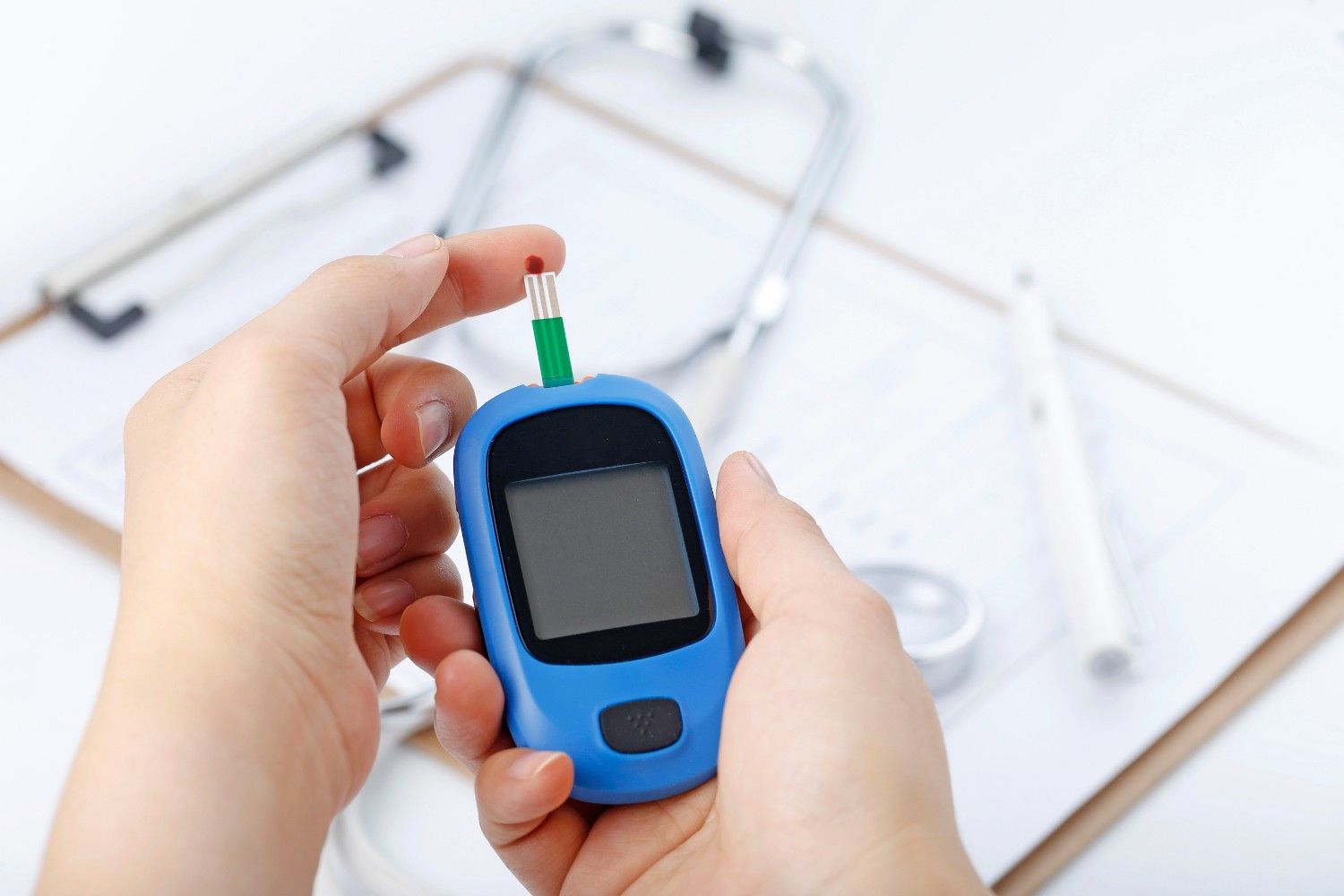 Hand holding a blood glucose meter measuring blood sugar, the background is a stethoscope and chart file - Ivf and Diabetes Concept